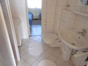 Das weiß geflieste Badezimmer mit geräumiger Duschkabine. Auch eine Waschmaschine für den kleinen Waschtag zwischendurch steht bereit. Eine Verbindungstür zum Schlafraum nach Osten öffnet den Blick auf die Ostsee.