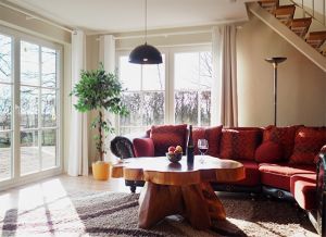 Der große und helle Wohnraum ist ausgestattet mit einem bequemen Ecksofa und Sessel mit Fußablage sowie einem urigen Couchtisch. Von hier gelangen Sie direkt auf die nach Süden gelegene Holzterrasse mit Blick auf grüne Wiesen und den Bodden – das Naturschutzgebiet Borner Holm.